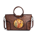 Sac en cuir bleu avec anses rondes, orné d’un médaillon illustrant un cerf stylisé, représentant le modèle Cervus Heritage
