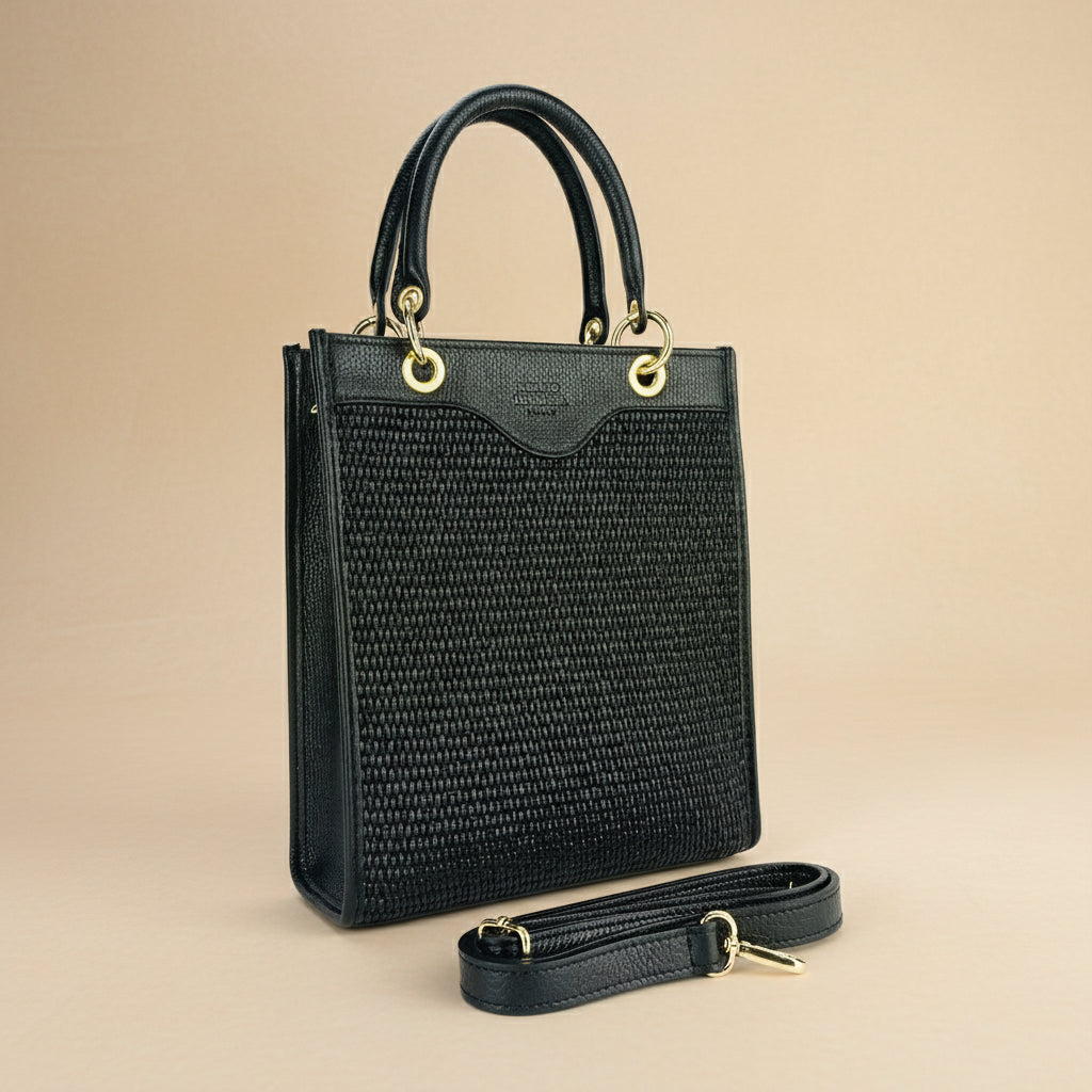 Sac vertical en cuir véritable et raphia noir, avec fermeture zippée, poignées renforcées, attache dorée, poche intérieure zippée et bandoulière amovible et réglable.