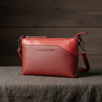 Pochette en cuir rouge lisse au format compact, dotée d’une fine bandoulière et pensée pour accompagner élégamment une soirée. 